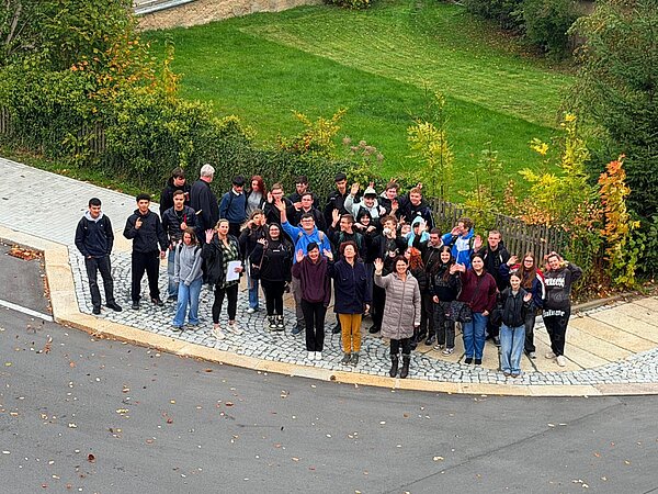 Schulgemeinschaft der Berufsschule Auerbach im Vogtland Gruppenfoto von Schülerinnen, Schülern und Lehrkräften der Berufsschule Auerbach, die im Freien stehen und teilweise in die Kamera winken.